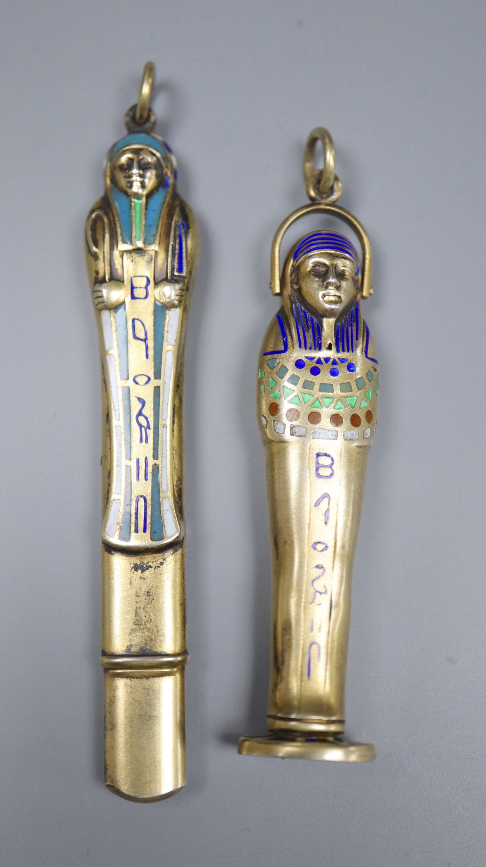 An early 20th century Egyptianesque gilt white metal and enamel propelling pencil/seal, 59mm and a similar pencil case, 72mm.